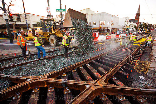 wheel loader dropping ballast on rail tracks, ballast, cat it38g, diamond crossing, front loader, gravel, high-visibility jacket, high-visibility vest, light rail, man, muni, ntk, railroad construction, railroad tracks, railway tracks, reflective jacket, reflective vest, safety helmet, safety vest, san francisco municipal railway, track maintenance, track work, tracks crossing, wheel loader, wheled loader, workers