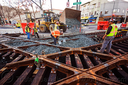 wheel loader drops ballast on rail tracks, ballast, cat it38g, diamond crossing, front loader, gravel, high-visibility jacket, high-visibility vest, light rail, man, muni, ntk, railroad construction, railroad tracks, railway tracks, reflective jacket, reflective vest, safety helmet, safety vest, san francisco municipal railway, track maintenance, track work, tracks crossing, wheel loader, wheled loader, workers