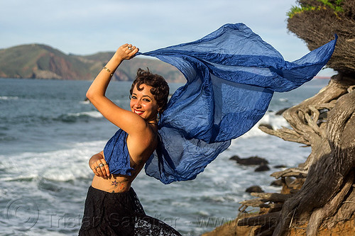 woman holding blue scarf in the wind on ocean shore, blue scarf, fashion, ocean, sea, seashore, tattoo, tree, wind, windy, woman, yassmine