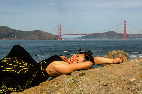 woman in black dress laying on rock near golden gate bridge, black dress, evening gowns, fashion, golden gate bridge, laying down, long dress, ocean, sea, seashore, sunbathing, suspension bridge, woman, yassmine