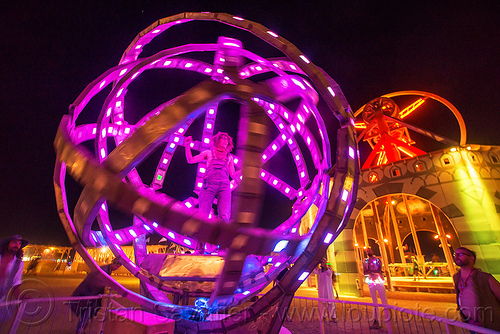 woman inside giant animated steel rings sculpture - burning man 2016, animated, art installation, burning man, disc-go-sphere, glowing, led light, night, sculpture, the man, woman