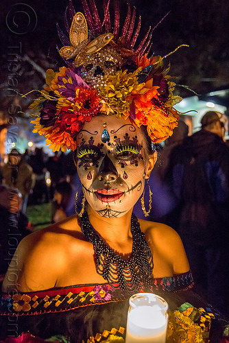 woman with sugar skull makeup and elaborate flower headdress - dia de los muertos, bindis, butterfly headdress, candle light, day of the dead, dia de los muertos, earrings, face painting, facepaint, fake eyelashes, flower headdress, glass candle, green eyelashes, halloween, necklace, night, sugar skull makeup, woman