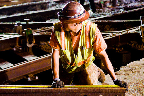 worker measuring rail with tape measure, high-visibility jacket, high-visibility vest, light rail, man, measuring tape, muni, night, ntk, railroad construction, railroad tracks, railway tracks, reflective jacket, reflective vest, safety helmet, safety vest, san francisco municipal railway, tape measure, track maintenance, track work, worker, working