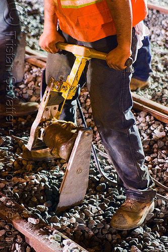 worker using railroad hand tamper - muni railway construction site (san francisco), ballast, gravel, hand tamper, high-visibility jacket, high-visibility vest, light rail, man, muni, night, ntk, power tool, railroad construction, railroad tracks, railway tracks, reflective jacket, reflective vest, safety vest, san francisco municipal railway, track maintenance, track work, worker, working