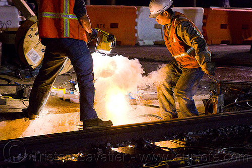 workers ignite cad-weld powder in a crucible, cad-welding, exothermic bonding, exothermic welding, high-visibility jacket, high-visibility vest, light rail, men, muni, night, ntk, railroad construction, railroad tracks, railway tracks, reflective jacket, reflective vest, safety helmet, safety vest, san francisco municipal railway, thermite welding, track maintenance, track work, welder, workers, working