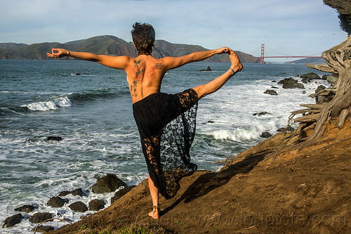 yoga - extended hand to big toe pose, balancing, black dress, black lace, butterfly tattoos, lace dress, ocean, one leg, rugged, sea, seashore, stretching, surf, white water, woman, yassmine, yoga