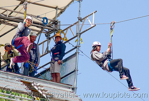 zoey riding the zip-line over san francisco, adventure, blue sky, cable line, cables, climbing helmet, embarcadero, hanging, jump, mountaineering, moving fast, speed, start, steel cable, tower, trolley, tyrolienne, urban, woman, zip line, zip wire