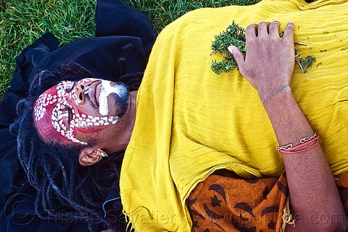 african shaman with tribal face paint, african american man, african face paint, black man, bracelet, dreadlocks, earring, eyes closed, eyes shut, face painting, facepaint, herbs, jason, lawn, laying down, makeup, red, redhead, tribal face paint, white, yellow tunic