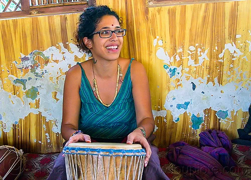 maryam with djembe drum, bindi, bracelets, djembe drum, drummer, eyeglasses, eyewear, maryam, musical instrument, necklaces, peeling paint, percussion, prescription glasses, rishikesh, sitting, spectacles, woman
