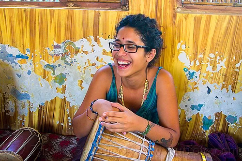 maryam with djembe drum, arm tattoo, bindi, bird tattoo, bracelets, djembe drum, drummer, eyeglasses, eyewear, maryam, musical instrument, necklaces, peeling paint, percussion, phoenix tattoo, prescription glasses, rishikesh, sitting, spectacles, tattoos, woman