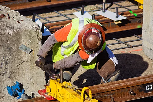 railroad construction worker adjusting a rail jack, construction worker, duboce, high-visibility jacket, high-visibility vest, light rail, men, muni, ntk, rail jacks, railroad construction, railroad tracks, railway tracks, reflective jacket, reflective vest, safety helmet, safety vest, san francisco municipal railway, track jacks, track maintenance, track work, working, wrench